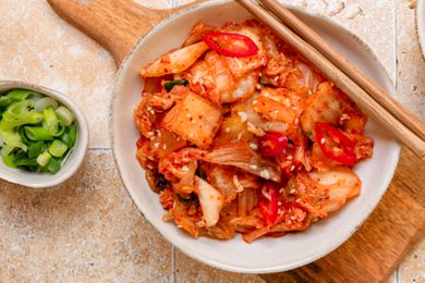 A bowl of kimchi with next to a smaller bow of chopped scallion