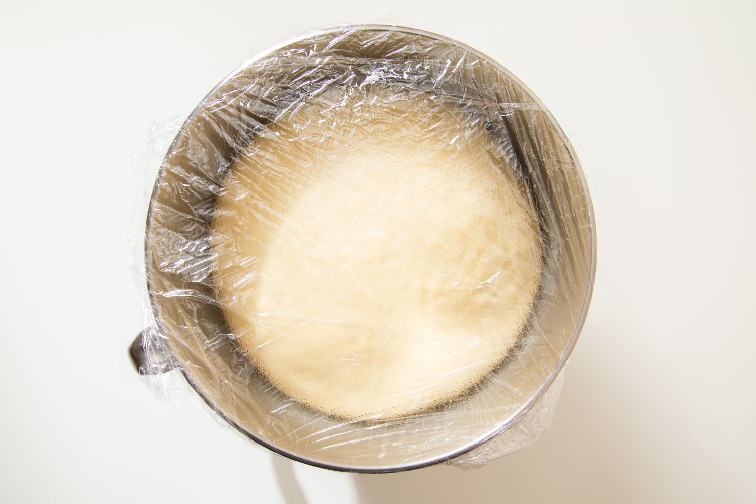 Salted honey rolls dough (doubled in size after resting) in a mixer bowl covered in plastic wrap
