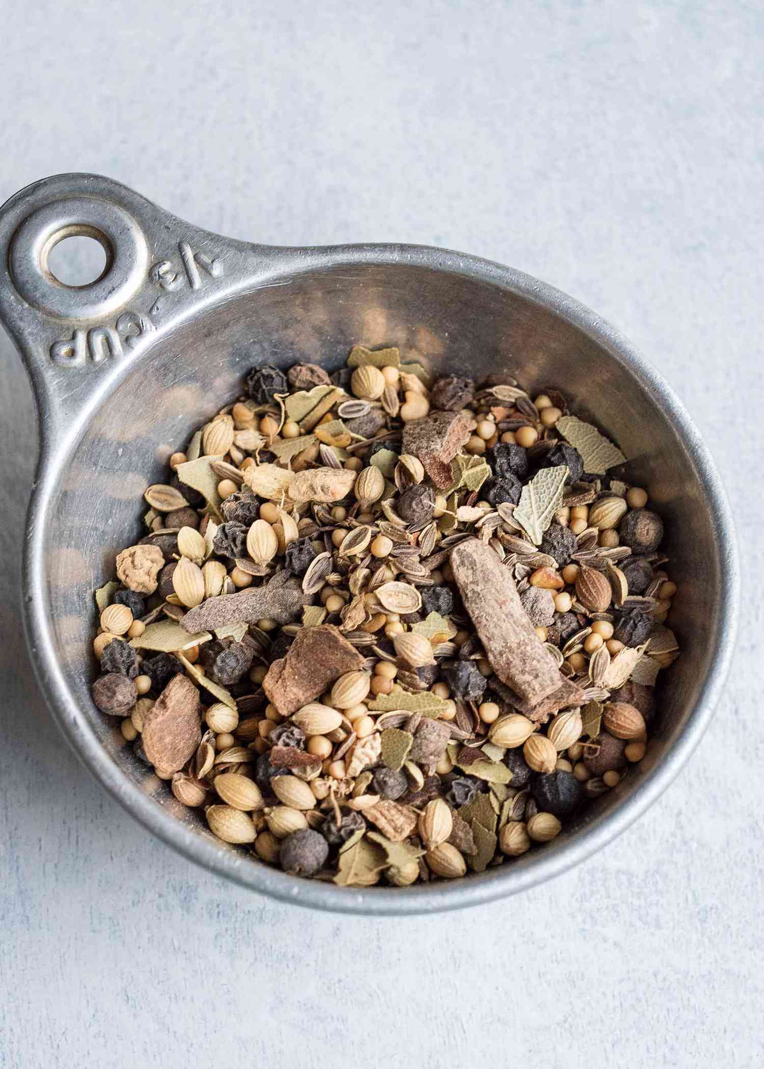 Pickling spice in a measuring cup: cinnamon, bay leaves, yellow mustard seeds, coriander seeds, black peppercorns, dill seeds, alspice berries, red pepper flakes