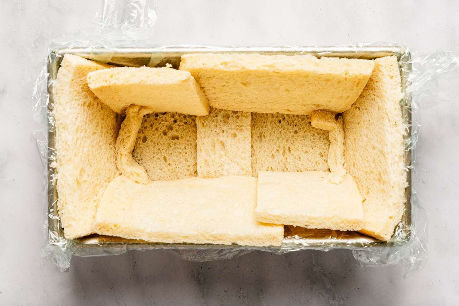 Overhead view of a metal bread baking pan with bread slices lining the inside for Easy British Summer Pudding recipe