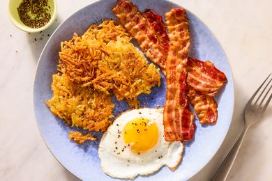 Plate with crispy hash browns sunnysideup egg and strips of cooked bacon