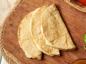 Three folded cheese quesadillas arranged on a wooden board