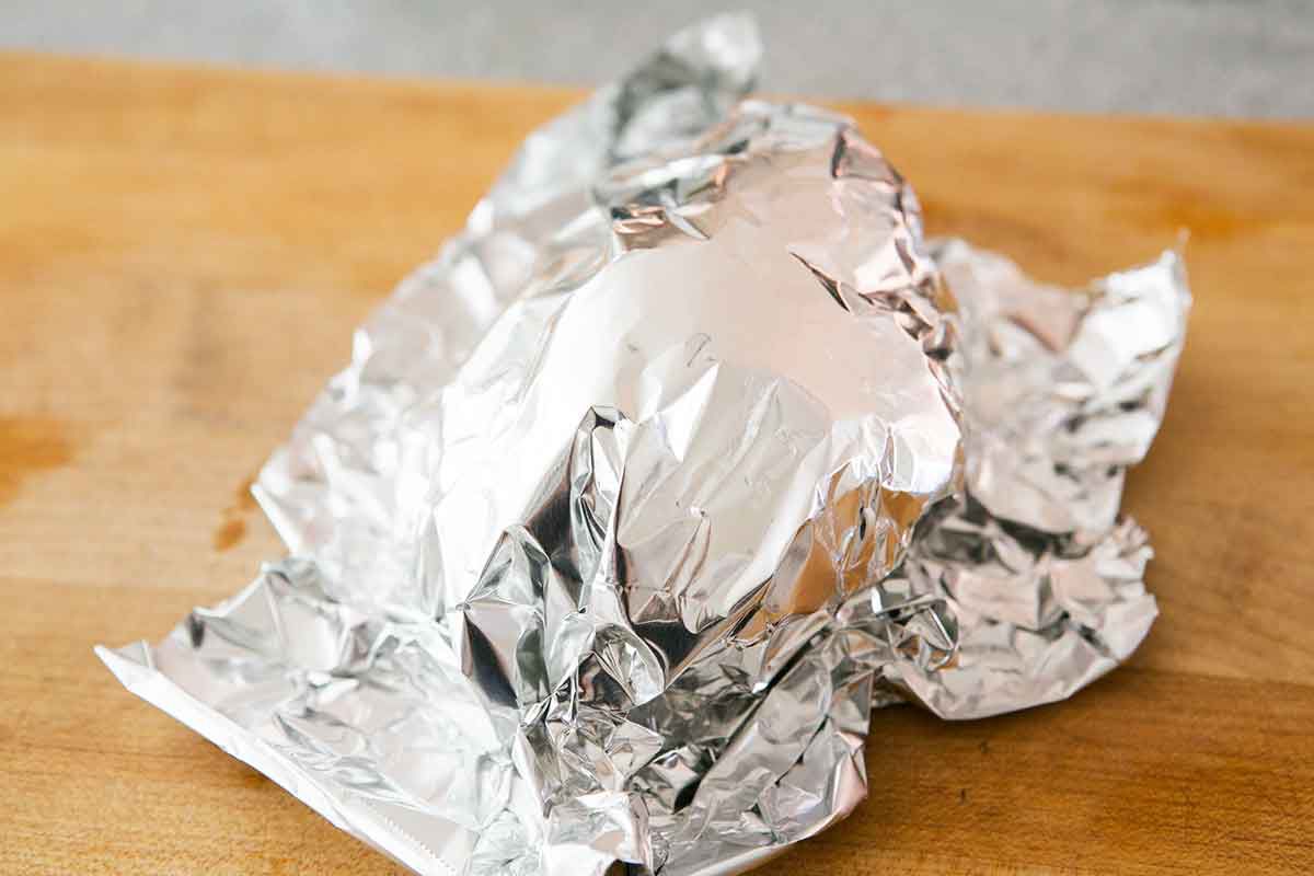 Cooked chicken covered in foil on a cutting board