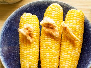 Three corn on the cobs on a plate topped with butter and spices