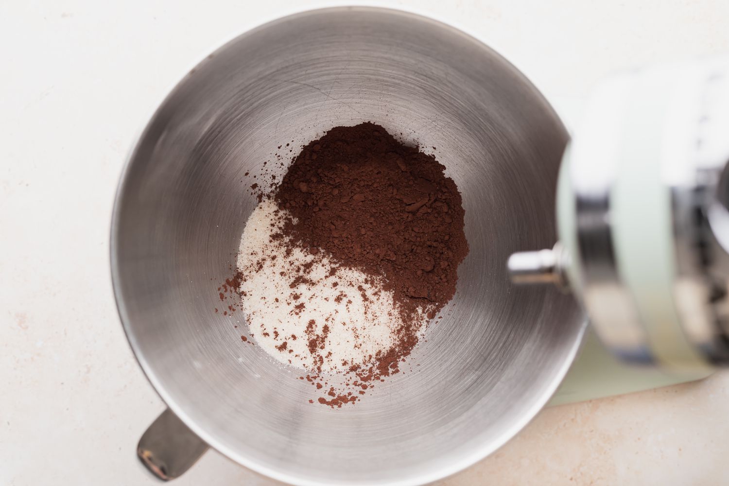 Cocoa powder, white sugar, and vegetable oil resting in a stand mixer