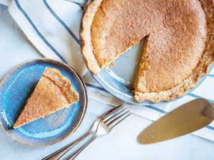 Overhead view of the best chess pie with a slice removed. The slice is on a blue plate with forks and a pie server to the right.