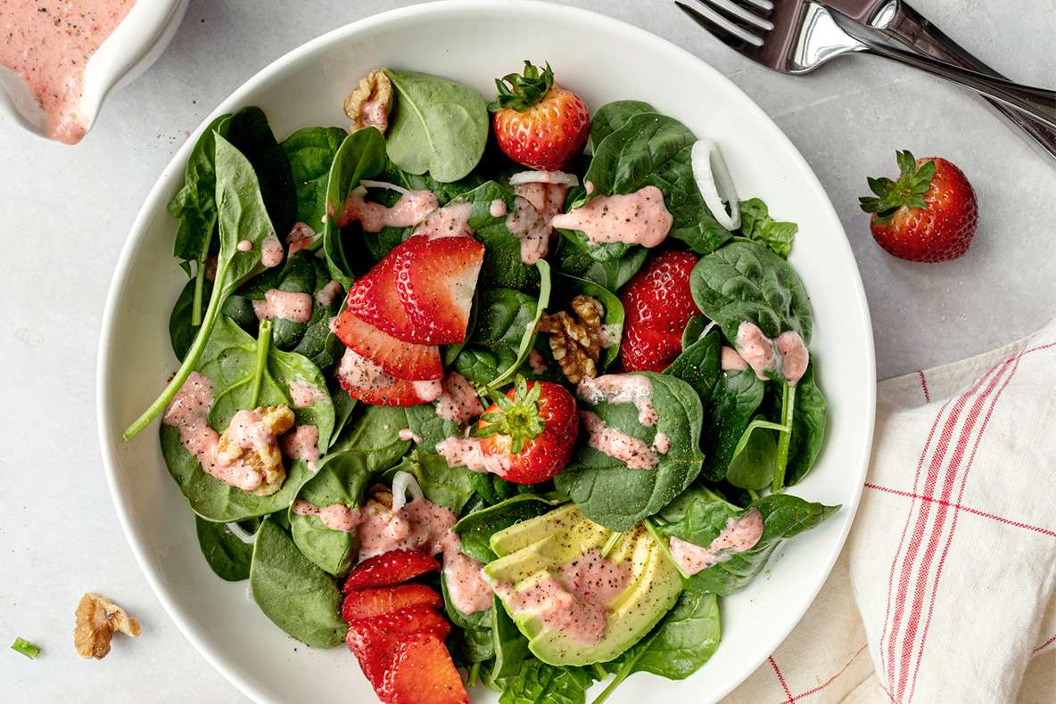 A spinach salad with strawberries walnuts avocado slices and a strawberry vinaigrette dressing drizzle