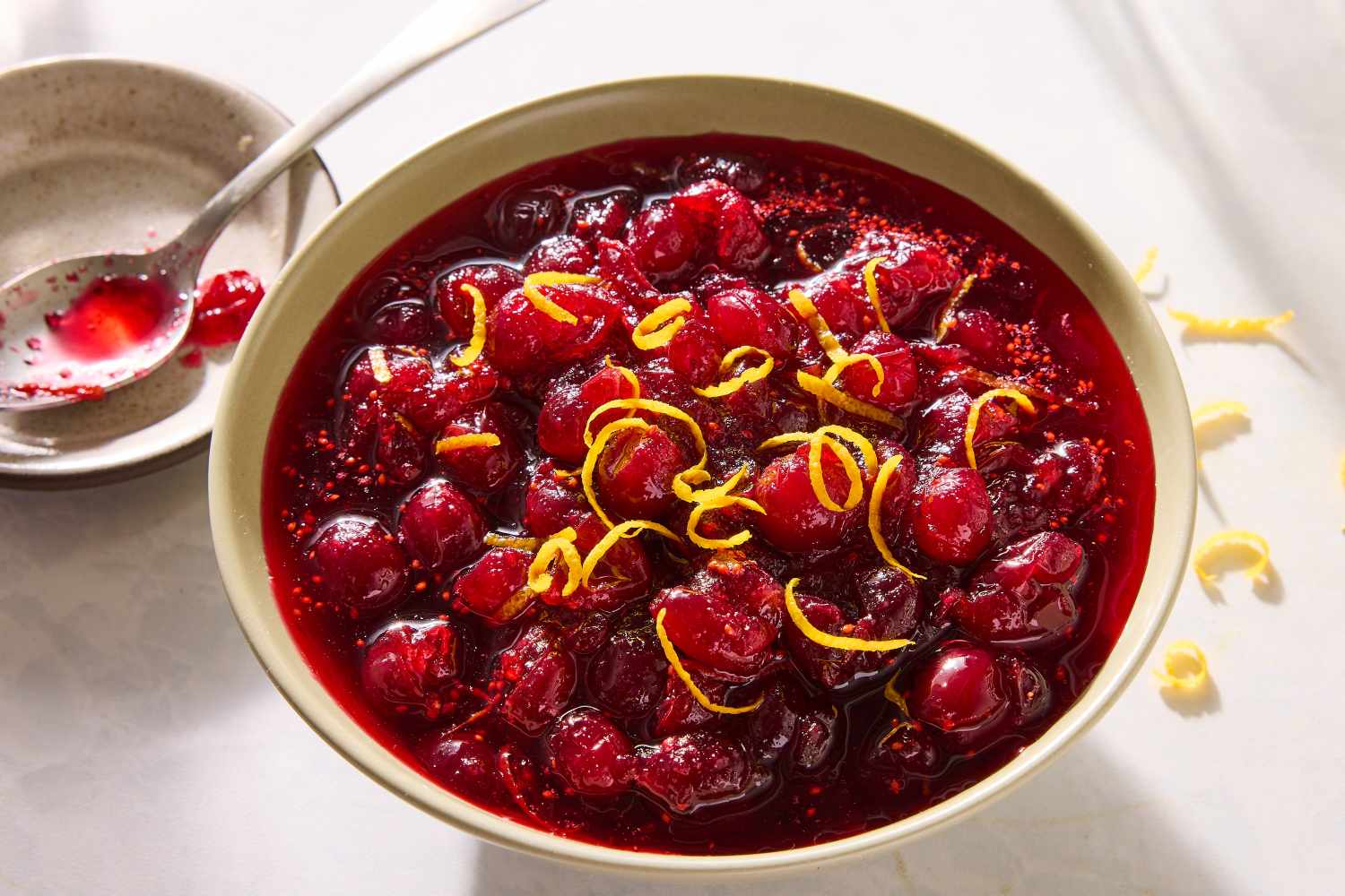 Bowl of cranberry sauce topped with grated zest with a spoon and bowl next to it
