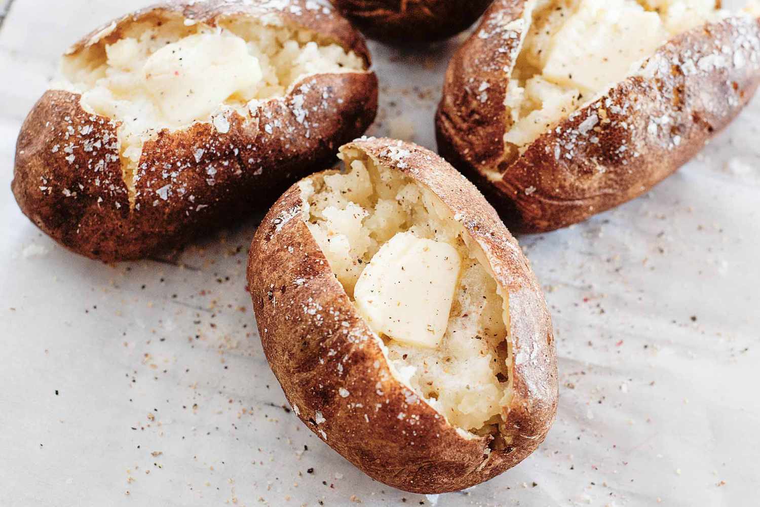 Three baked potatoes, split open with butter, salt, and pepper