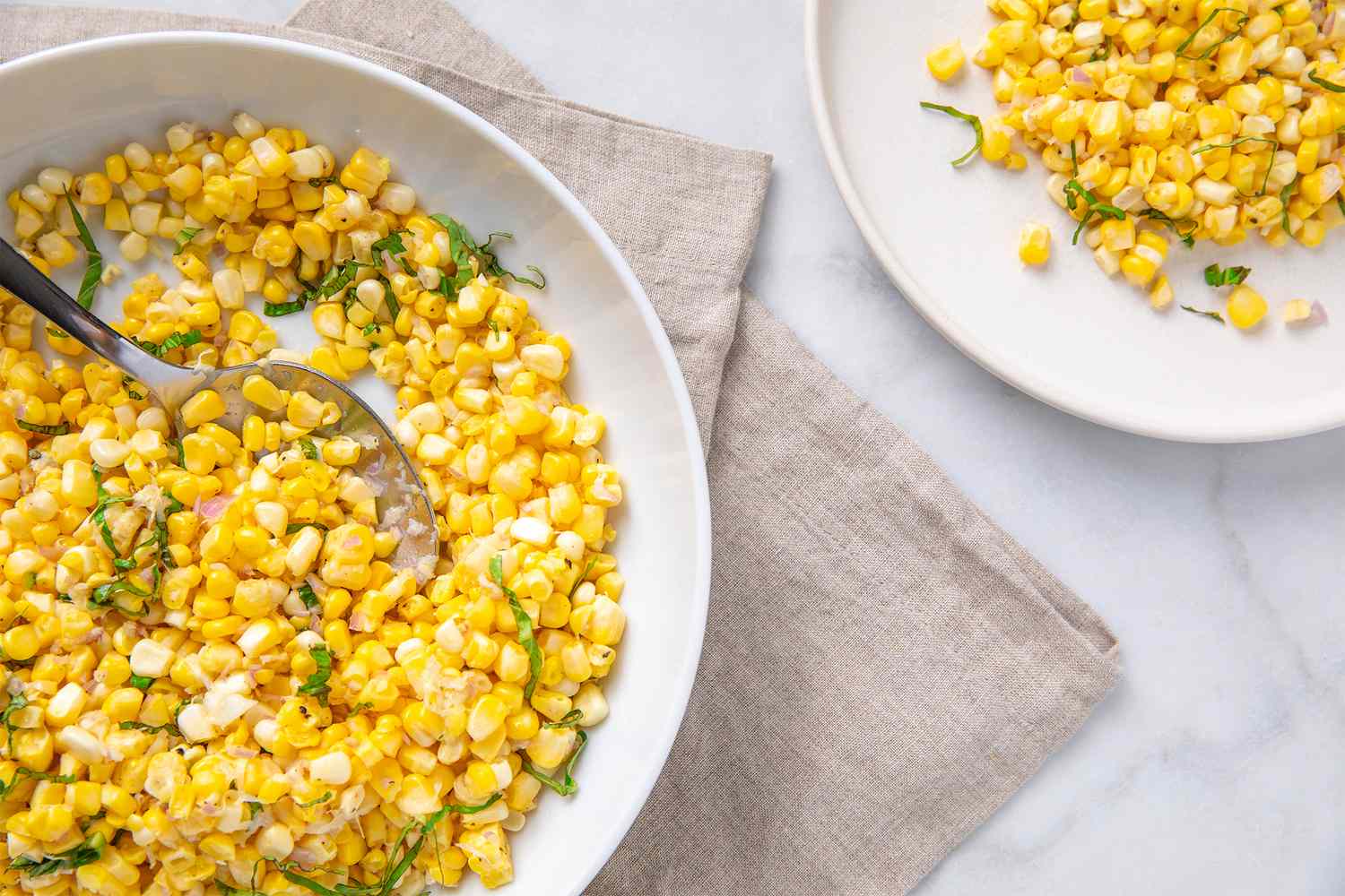 Plate with a corn salad featuring chopped herbs and a spoon garnished with toppings