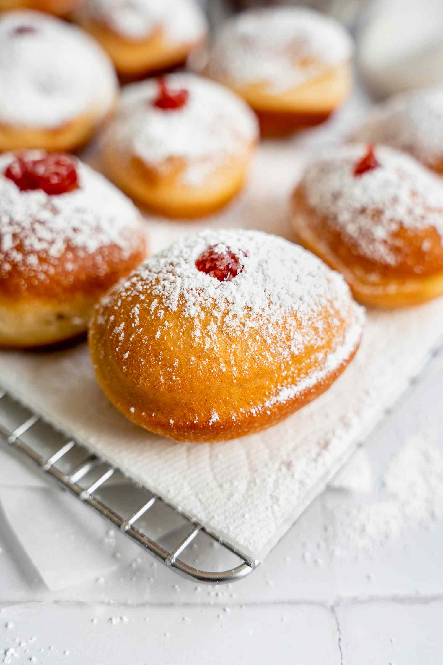 Sufganiyot (Israeli Jelly Donuts) on a Paper Towel Lined Cooling Rack Sitting on Parchment Paper