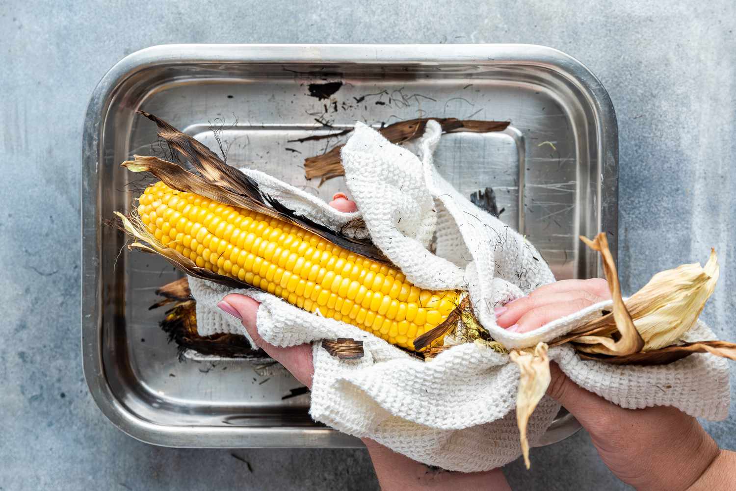 Corn Husk Carefully Removed from Grilled Corn on the Cob Using a Kitchen Towel