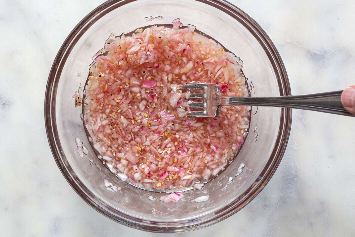 Overhead view of a glass bowl and fork making mignonette sauce.