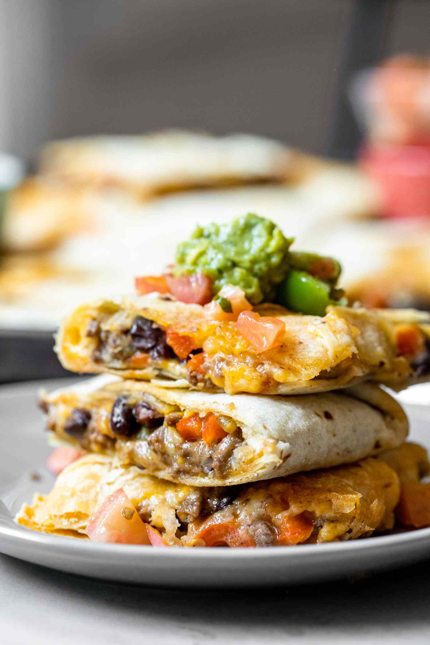 Stack of Loaded Sheet Pan Quesadillas Pieces on a Plate Topped with Salsa and Guacamole