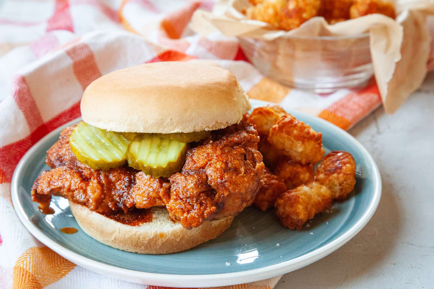 Nashville hot chicken sandwich with pickles and served on a plate.