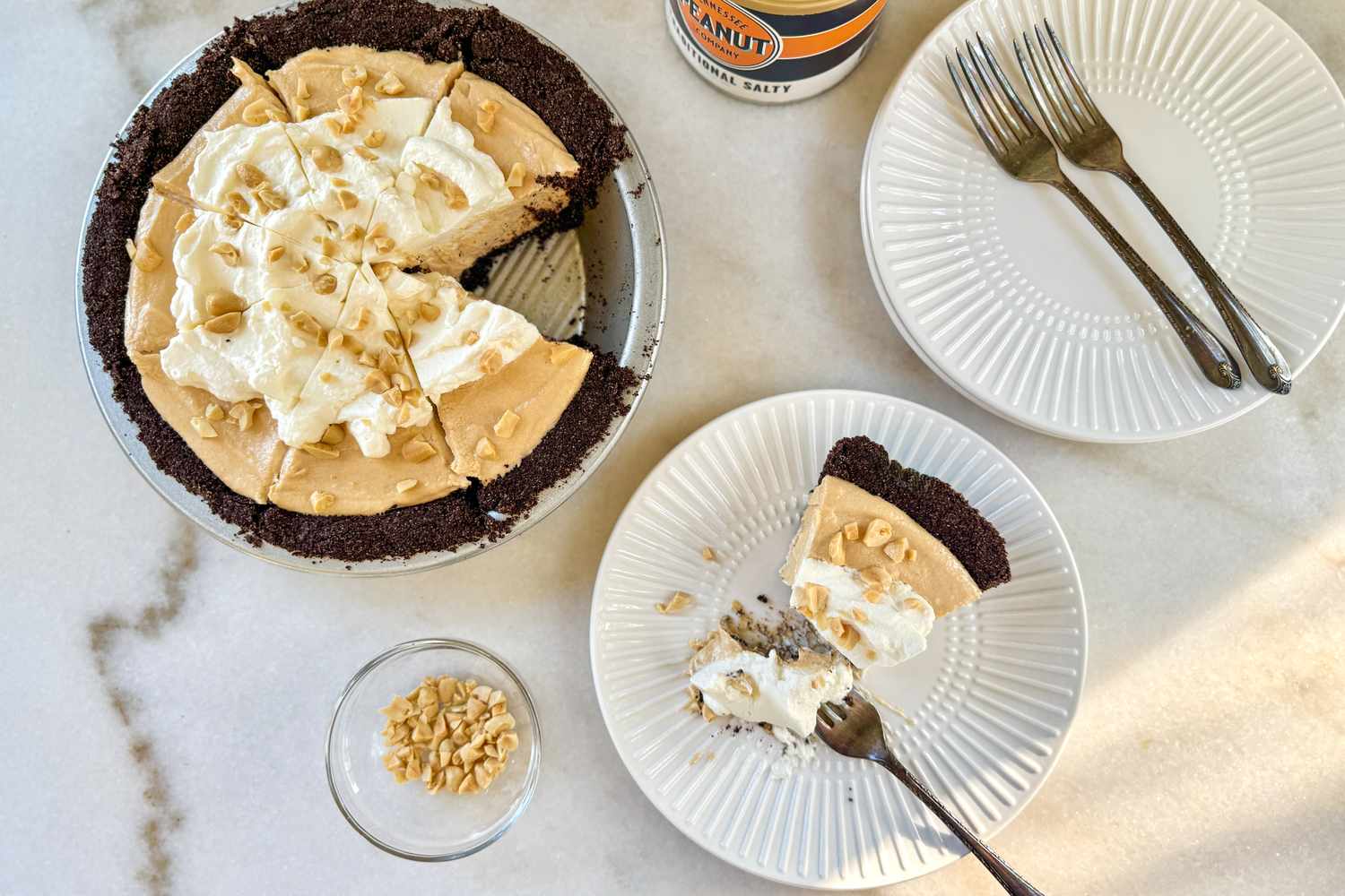 A peanut butter pie with whipped topping and a sliced serving on a plate garnished with crushed peanuts