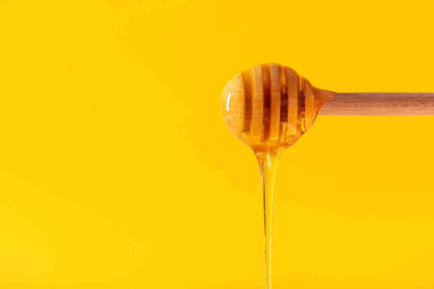 Wooden honey dipper with honey against yellow background