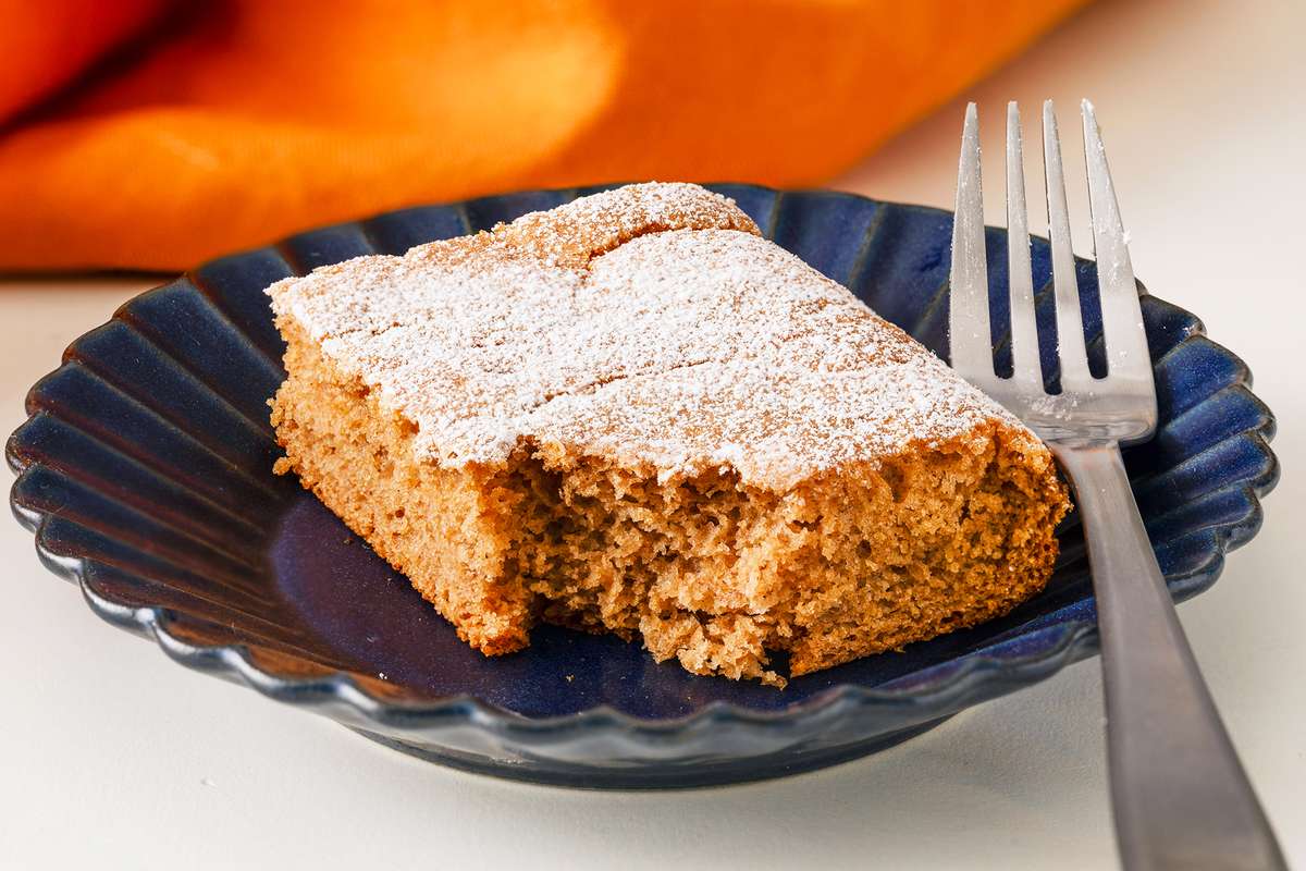 A slice of soda cake topped with powdered sugar on a blue plate accompanied by a fork