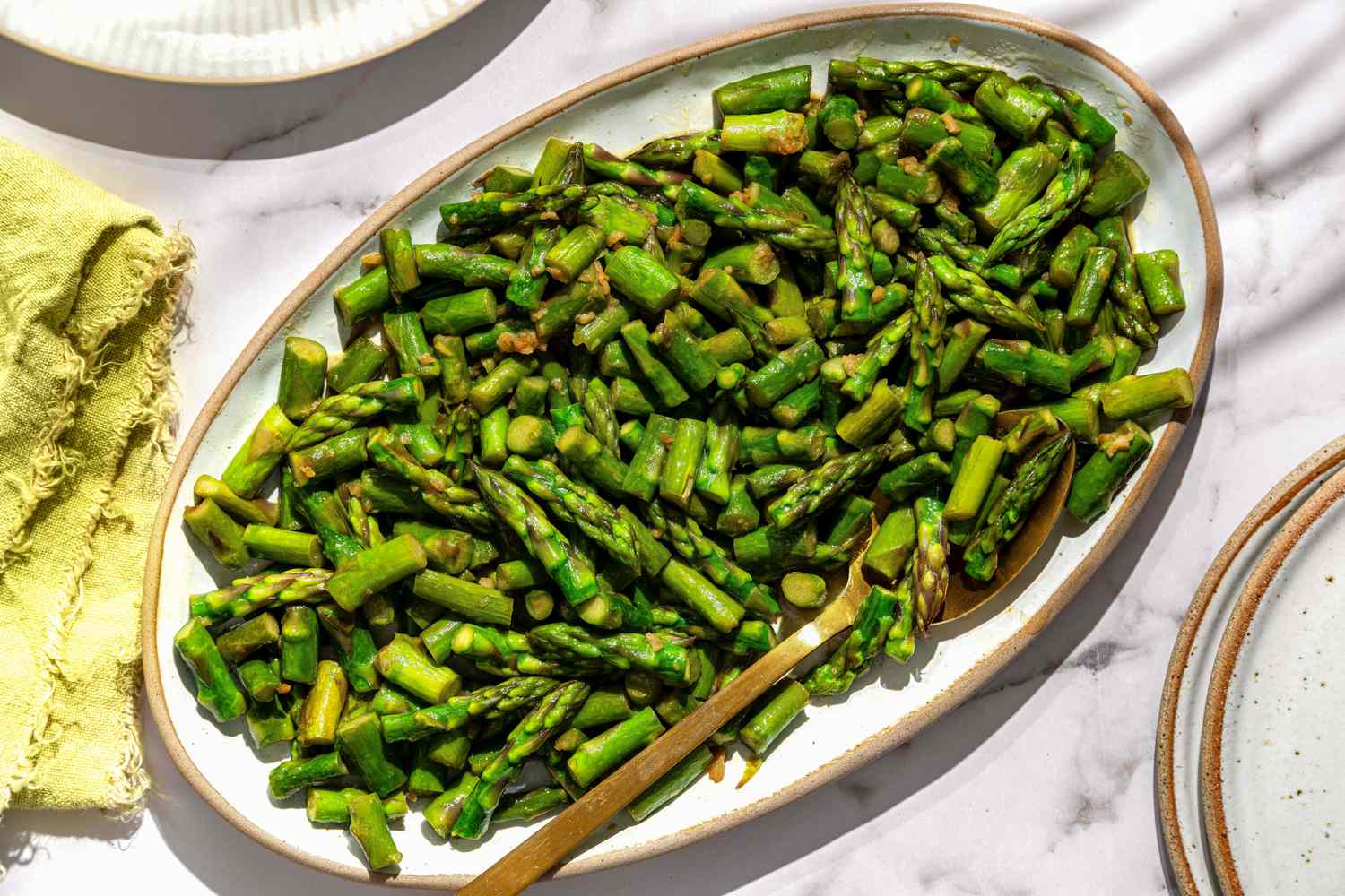 Sautéed asparagus on a serving platter with a wooden spoon.