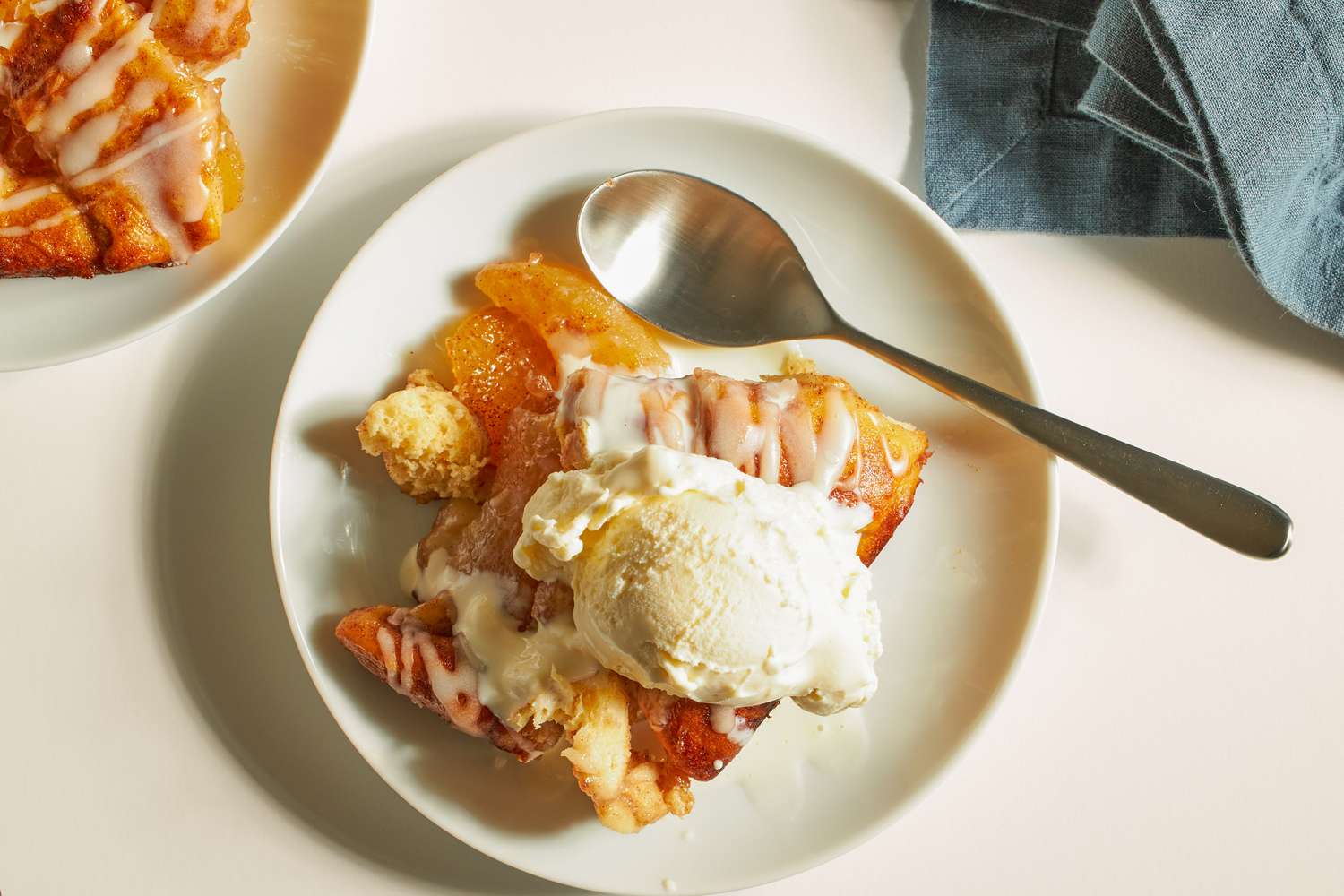 A plate of dessert featuring cinnamon roll and ice cream served with a spoon