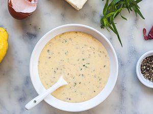 Overhead view of Béarnaise sauce with shallots, herbs, and lemon around the bowl.