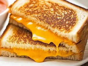 Grilled cheese sandwich with melted cheese served on a plate accompanied by a bowl of tomato soup in the background