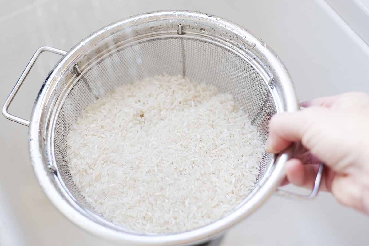 White rice being rinsed in a colander in the sink