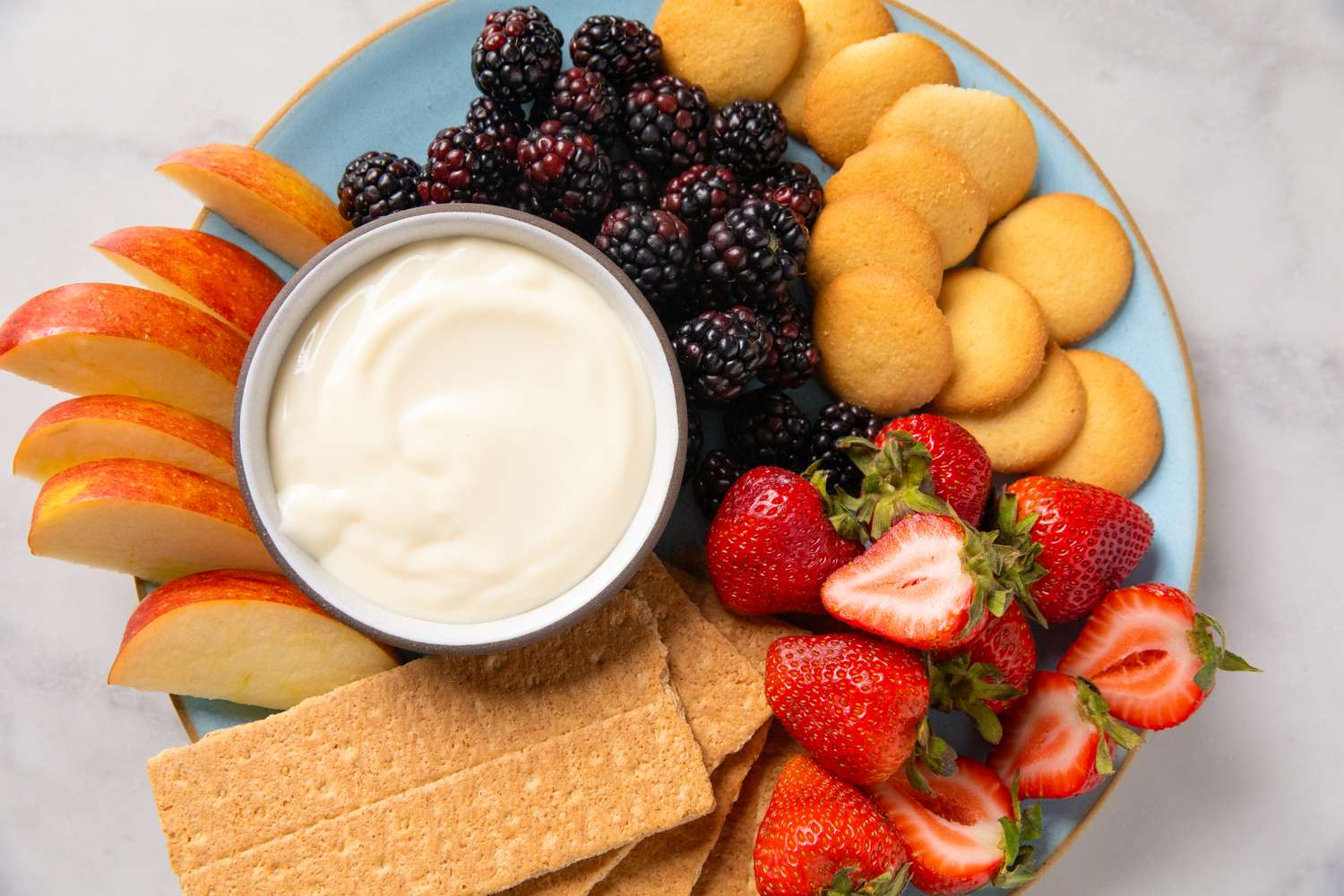 A plate with cheesecake dip fruits and cookies arranged for serving