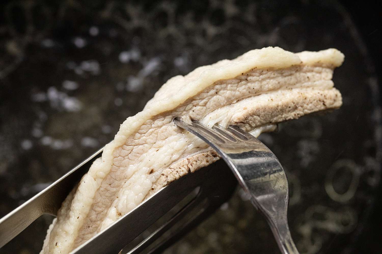 Fork Poking Slab of Pork to Check if Tender for Pancit Bihon (Filipino Rice Noodles) Recipe