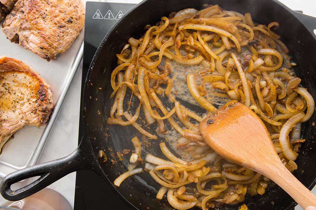 Onions sauteed in a cast iron skillet with a wooden spoon.