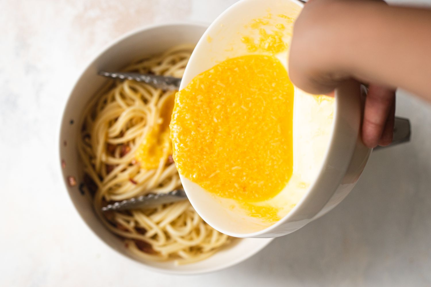 Adding whisked eggs to a bowl of noodles for Spaghetti Carbonara.