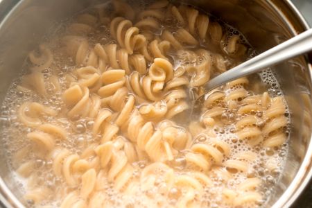 Pasta cooking in a pot with a utensil stirring it