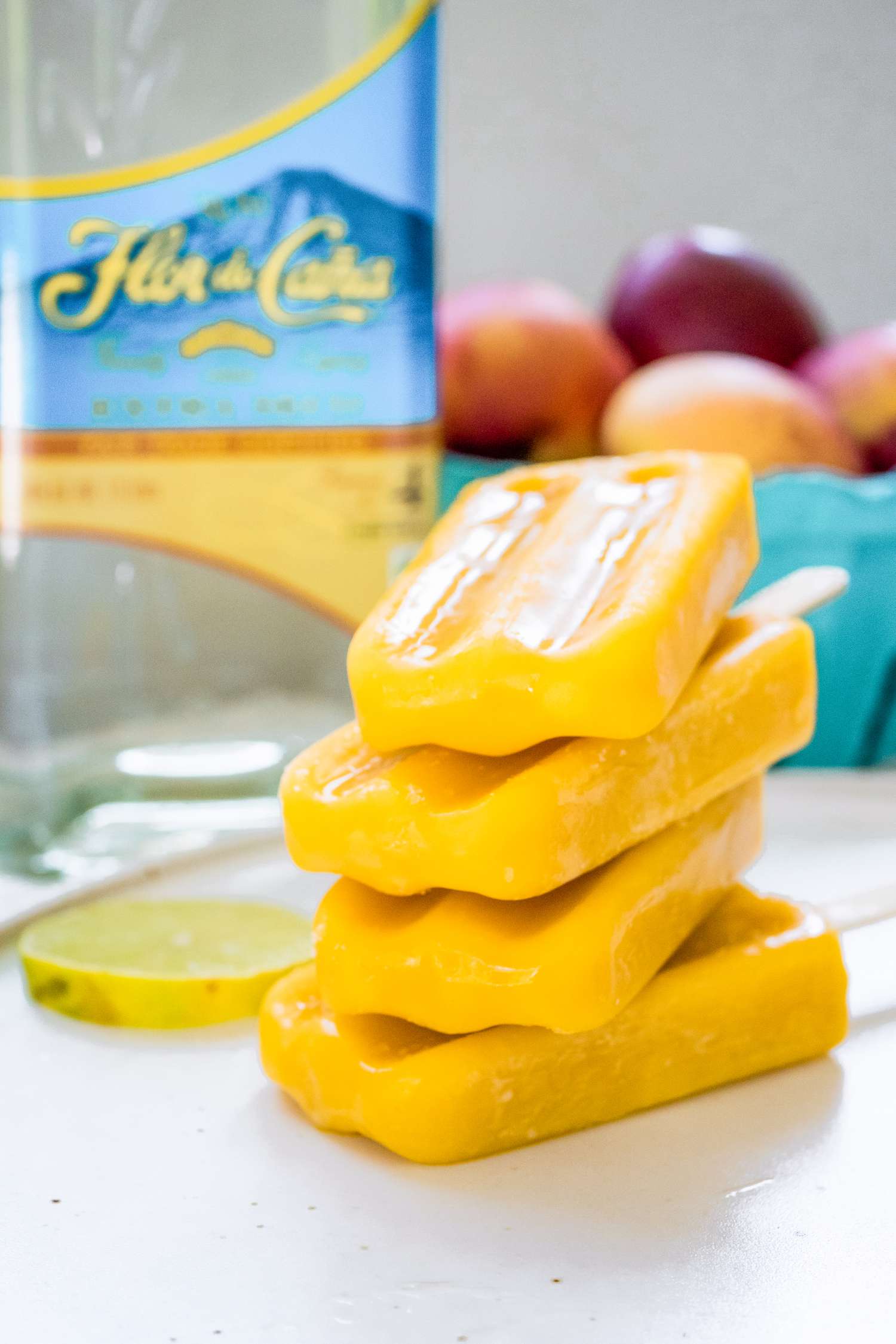 Peach Daiquiri Popsicles Stacked on a Plate with Ingredients in the Background