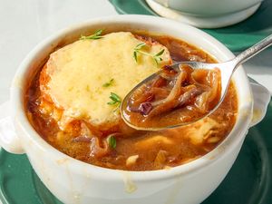 A bowl of French onion soup topped with melted cheese and herbs served with a spoon