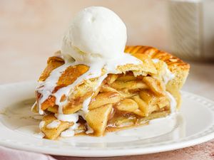 Slice of apple pie topped with a scoop of vanilla ice cream on a white plate