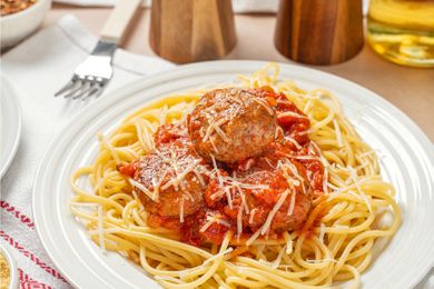 Plate of spaghetti with meatballs and tomato sauce topped with grated cheese