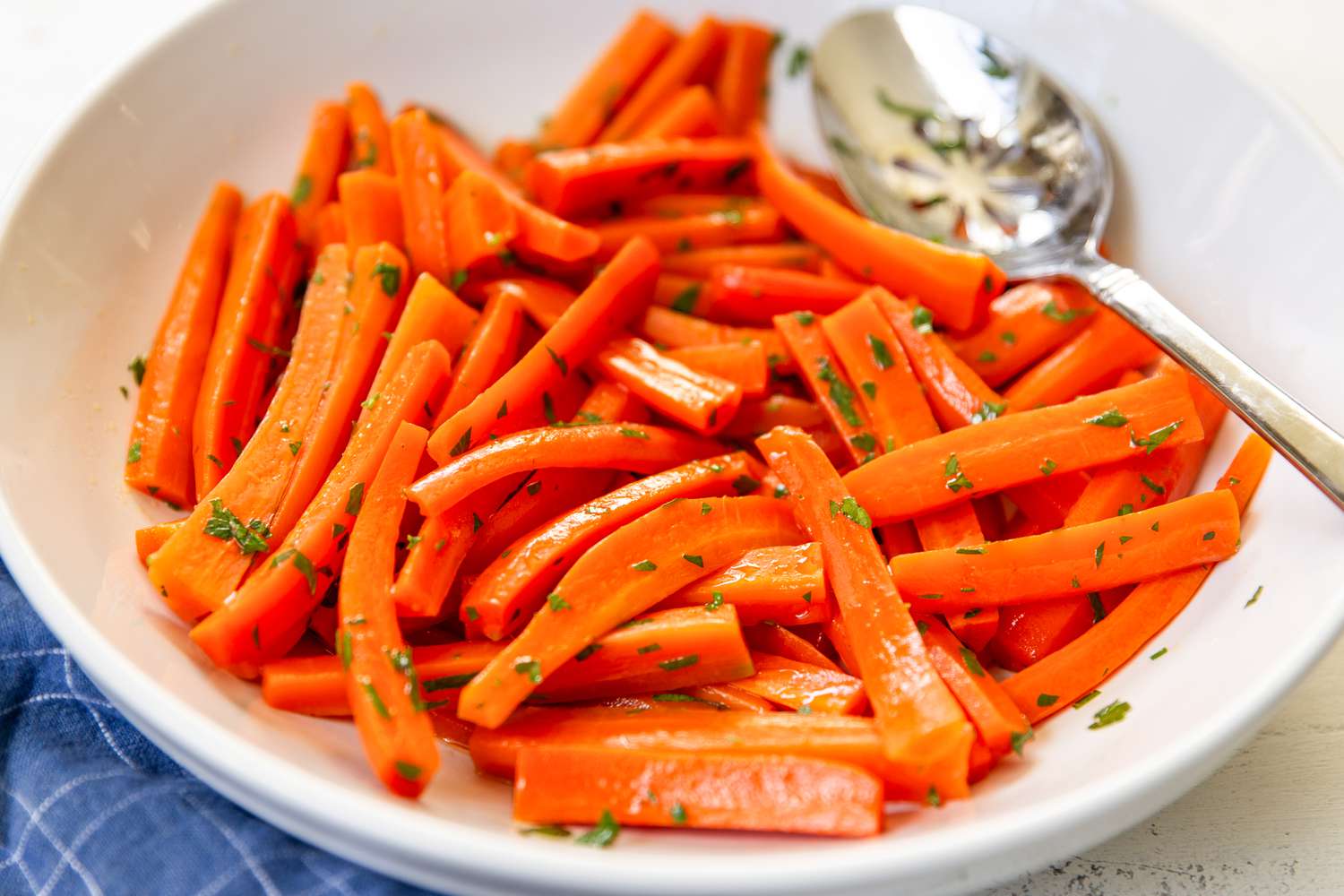 Closeup of julienned carrots tossed in herbs in a white shallow bowl with a serving spoon