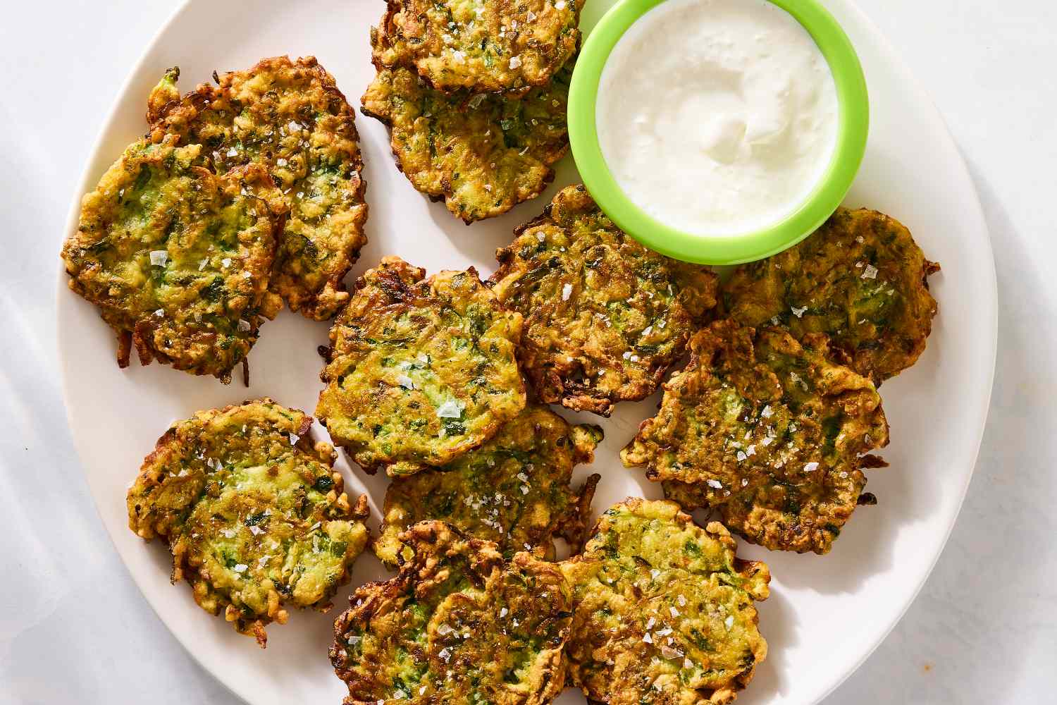 A plate of zucchini fritters next to a dipping sauce