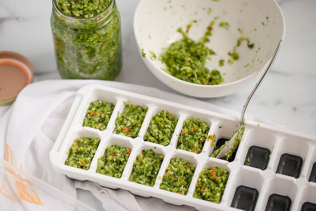 Carribbean green seasoning spooned into an ice tray and more in a jar