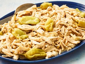 Angled view of a blue platter and a serving spoon with shredded chicken and pepperoncini