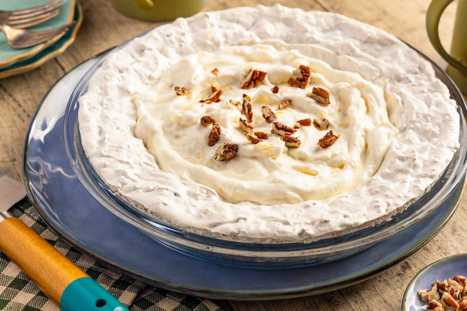 Angled view of a cream pie topped with pecans in a clear glass pie plate resting on a blue plate and a wooden tabletop