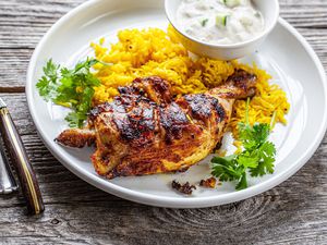 Grilled Tandoori Chicken with Turmeric Rice on Plate Next to Bowl of Raita