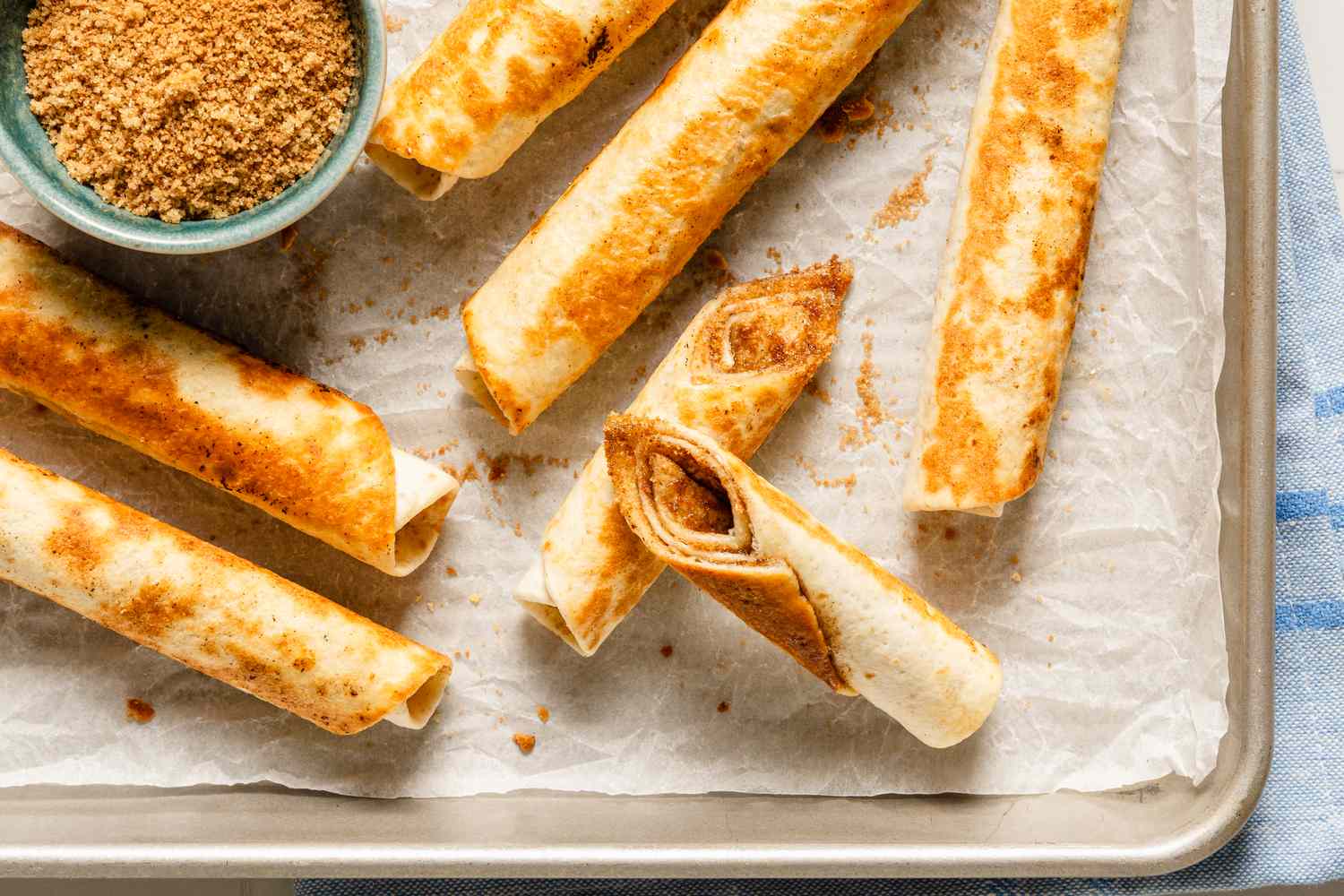 Cinnamon sugar roll-ups arranged on parchment paper with a bowl of brown sugar
