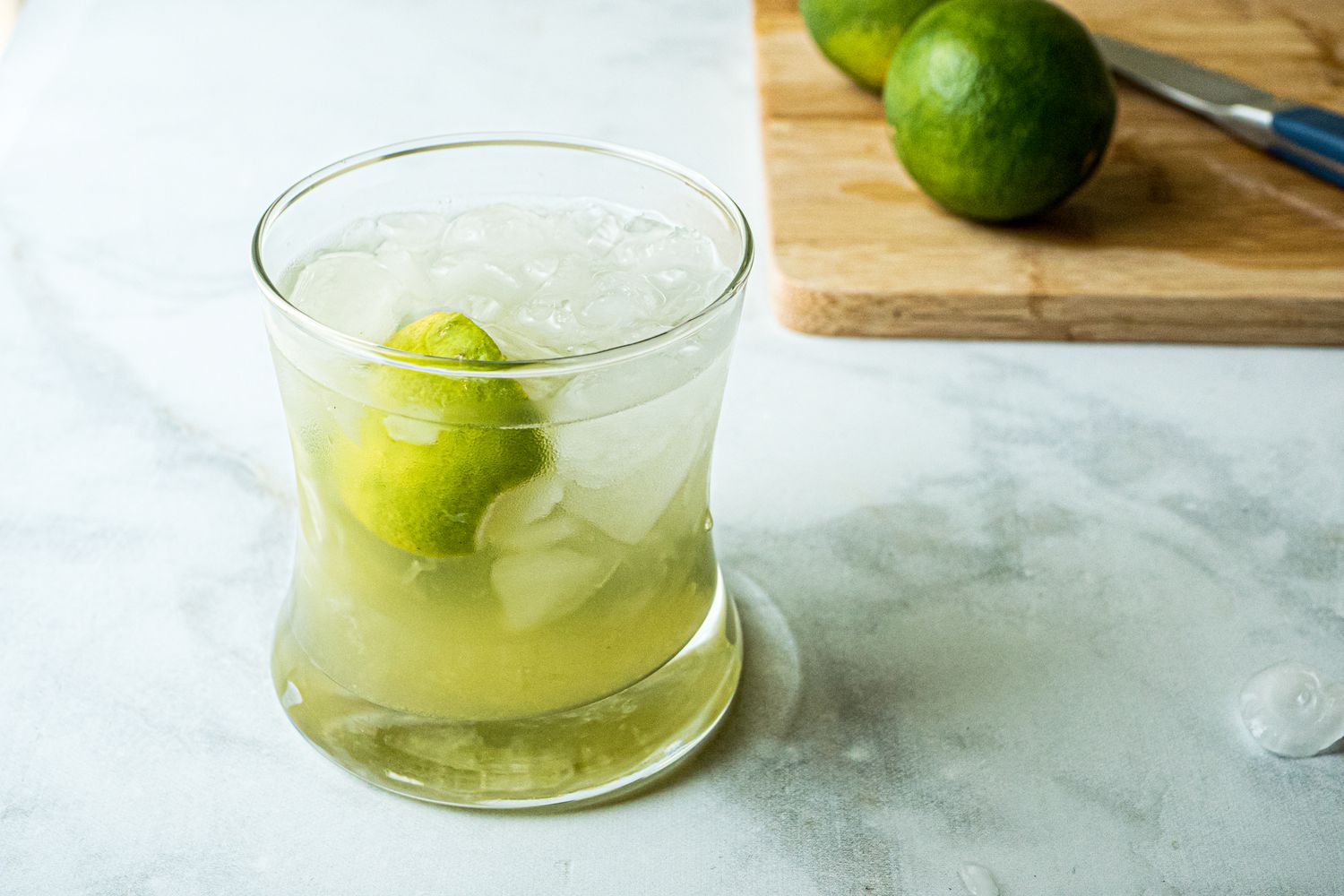 Brazilian caipirinha with a lime on a cutting board behind it.
