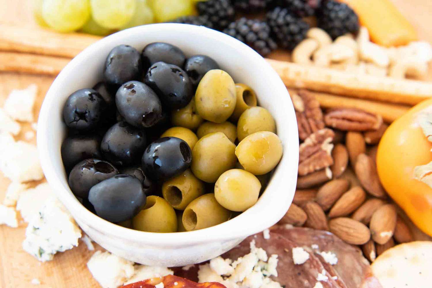 Green and black olives in a bowl on a cheese board