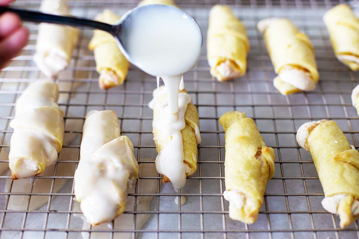 Glaze being spooned over baked Butterhorn Christmas Cookies.