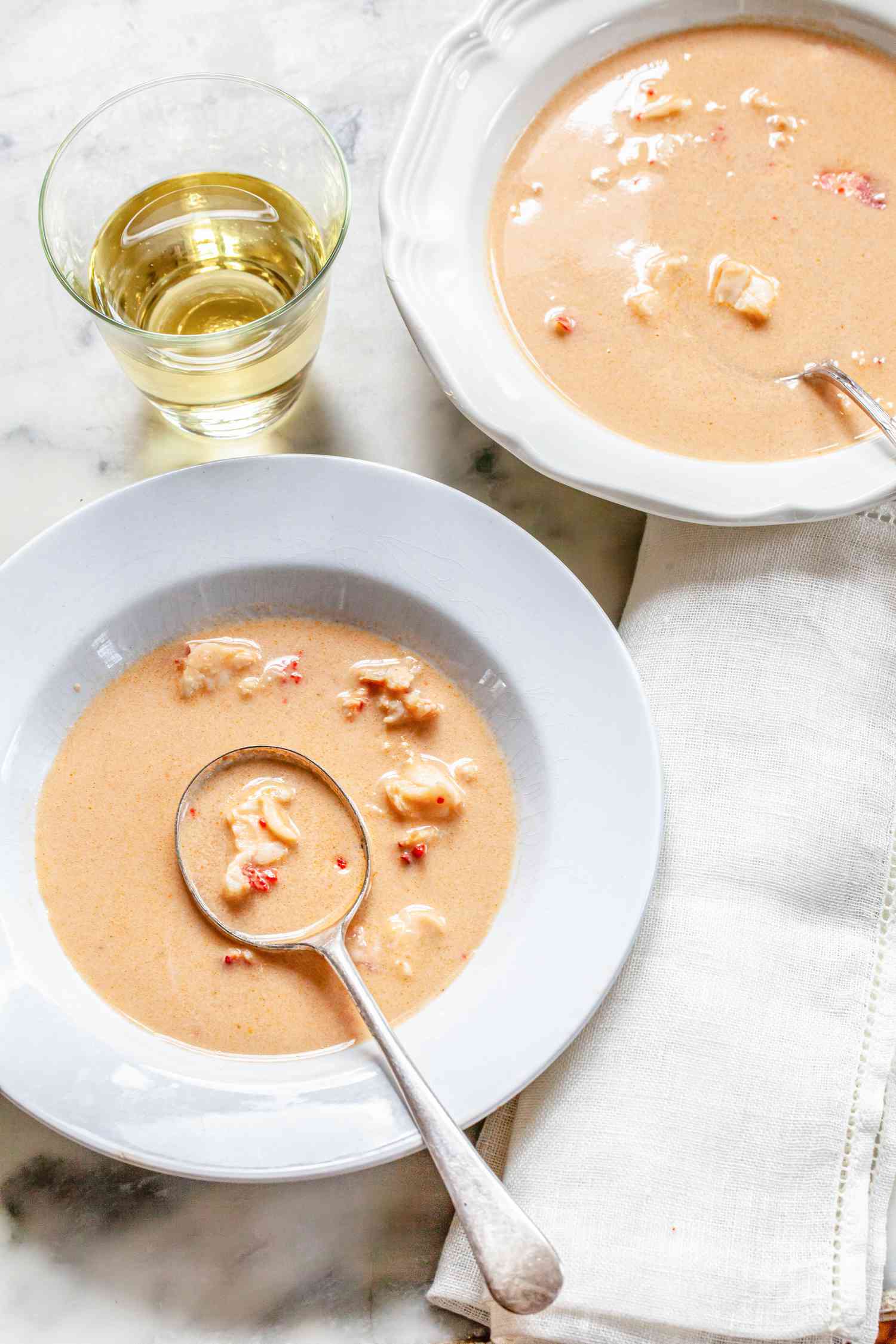 Two Bowls of Lobster Bisque Next to a Table Napkin and a Glass