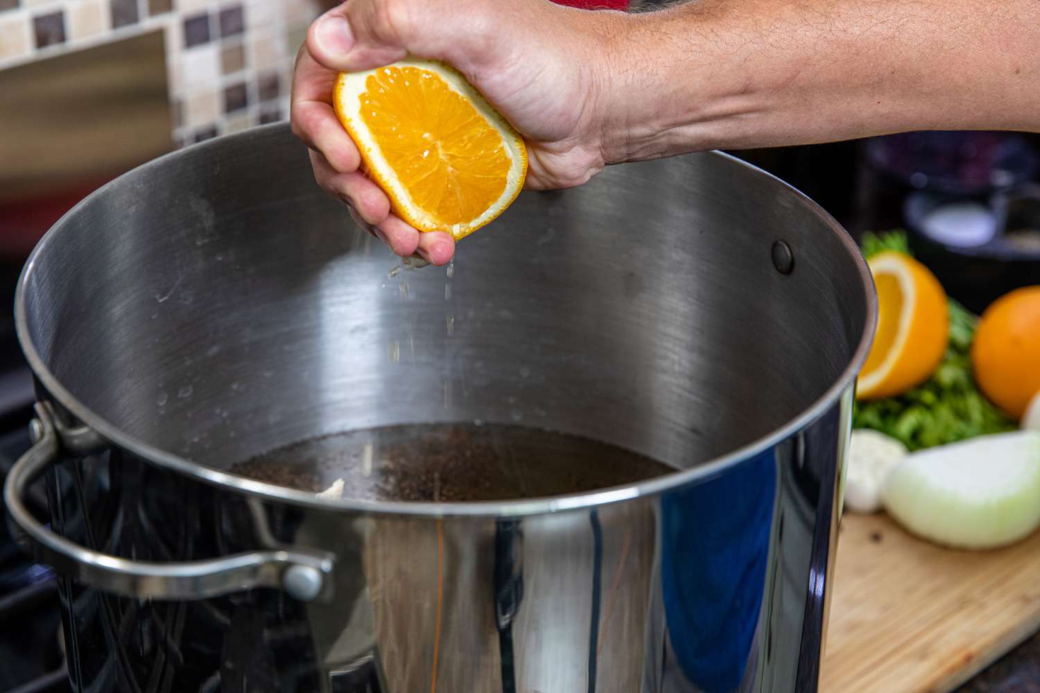 Squeezing orange sections into a pot to make a citrusy brine for whole turkey.
