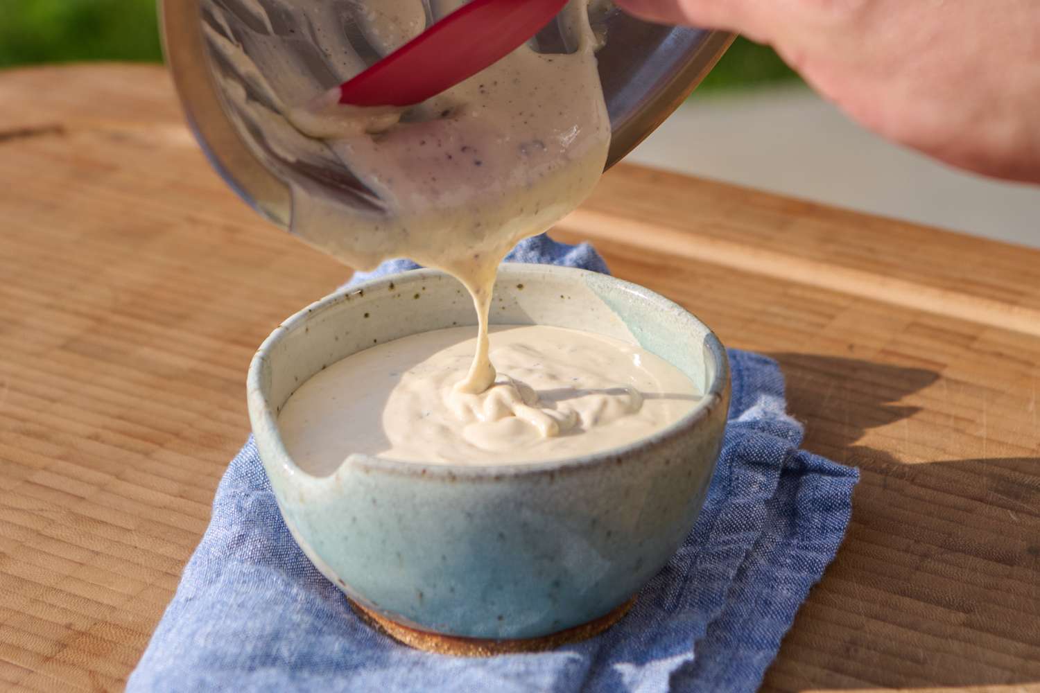 Sauce being poured into a ceramic bowl on a wooden surface with a blue cloth underneath