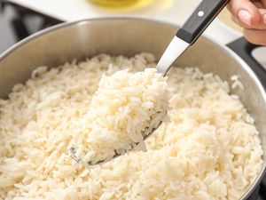 Closeup of a spoon with cooked rice above a pot with cooked rice